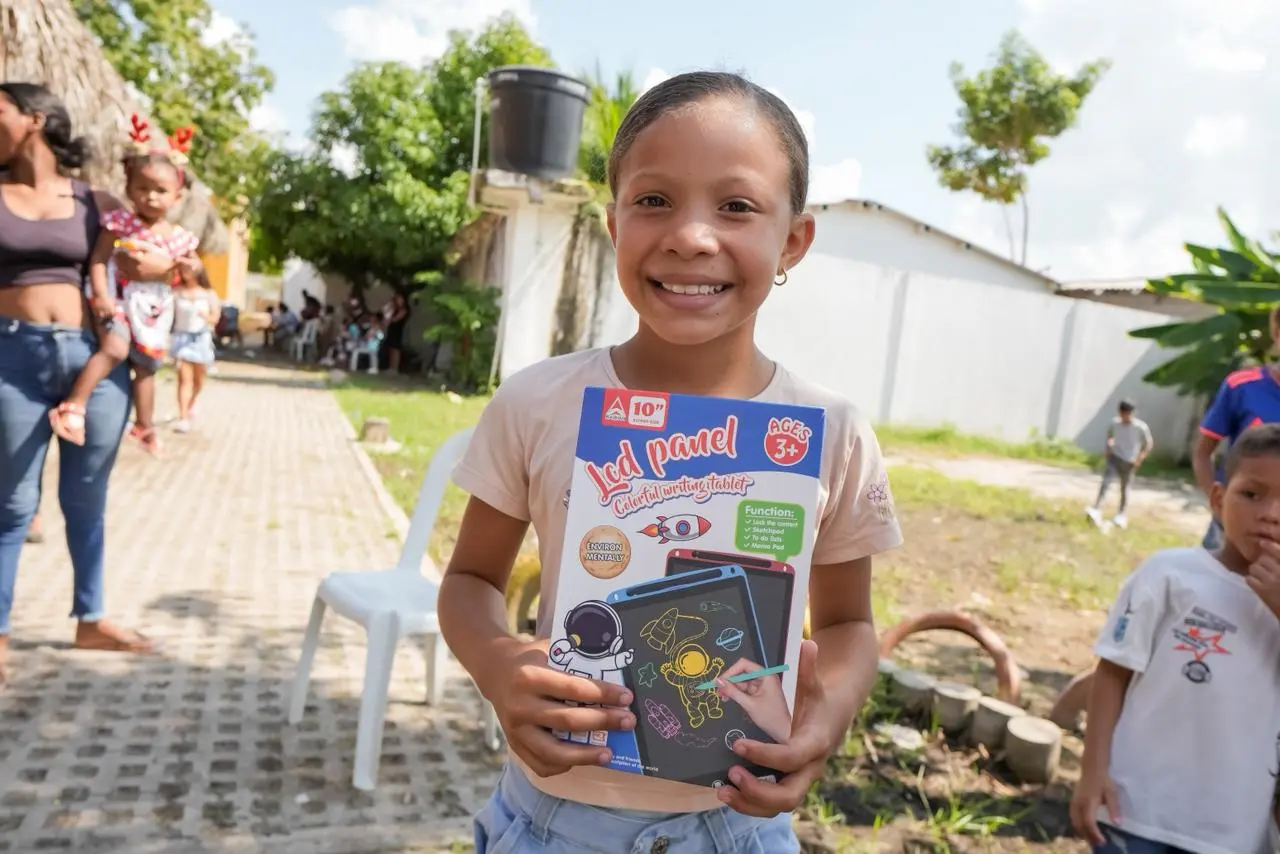 Niña sonríe y muestra un obsequio recibido en Bolívarland