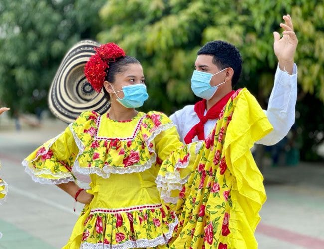 Pareja de bailarines con trajes típicos del Caribe colombiano realizando una danza folclórica mientras utilizan tapabocas al aire libre.
