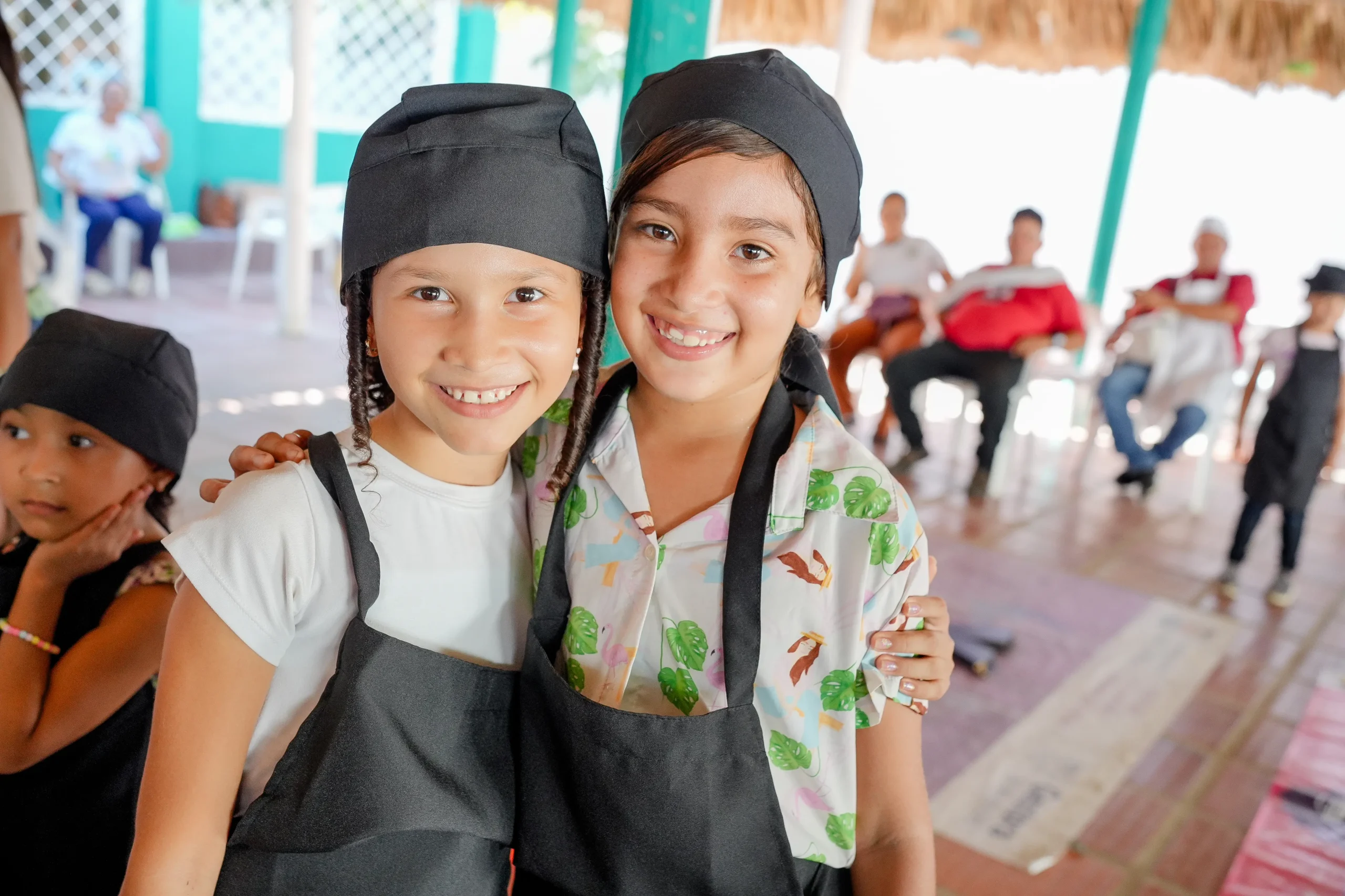 Dos niñas sonríen con delantales y gorros de cocina