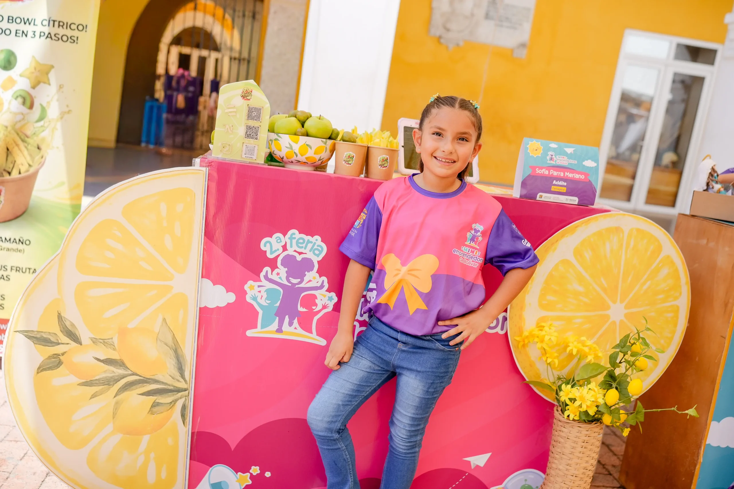 Niña presenta su emprendimiento en un puesto decorado con frutas