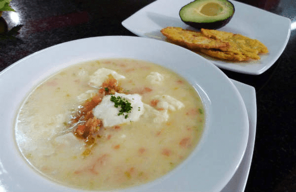 Plato de mote de queso con queso costeño flotante, acompañado de patacones y aguacate, sopa tradicional del Caribe colombiano.