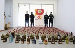 Botellas de licor incautadas alineadas en el piso frente a funcionarios y un aviso del programa Anticontrabando.