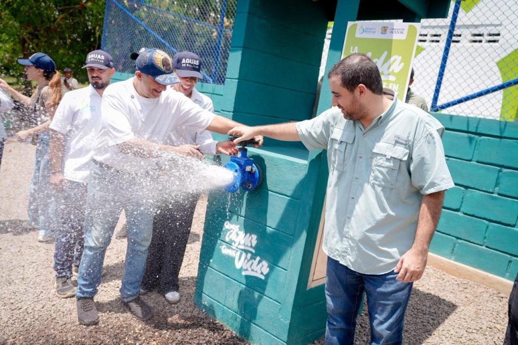 Dos hombres abren una llave de agua durante la inauguración del acueducto, mientras otros observan.