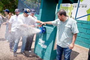 Dos hombres abren una llave de agua durante la inauguración del acueducto, mientras otros observan.