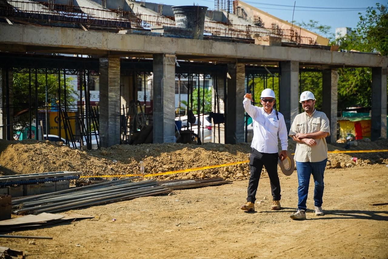 Dos hombres con casco blanco recorren la obra de un estadio de béisbol en construcción.