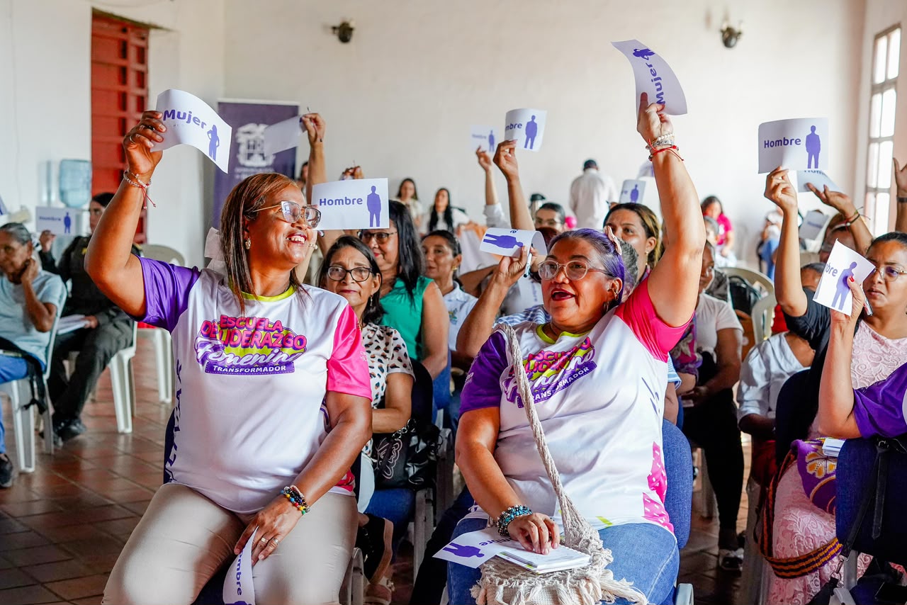 Mujeres sentadas levantan tarjetas con las palabras Mujer y Hombre durante una dinámica del taller.
