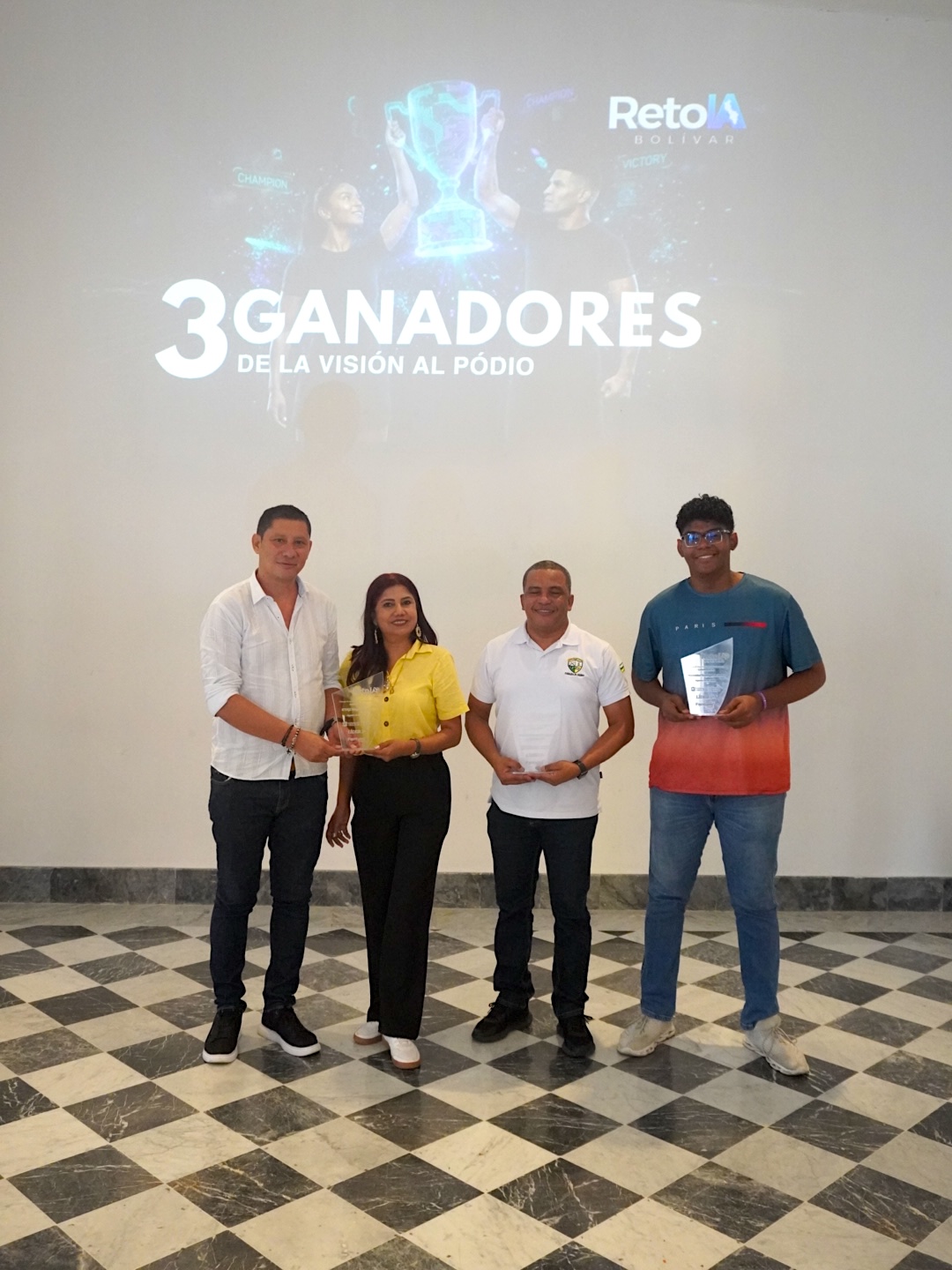 Cuatro personas posan con reconocimientos frente a una pantalla que anuncia tres ganadores.
