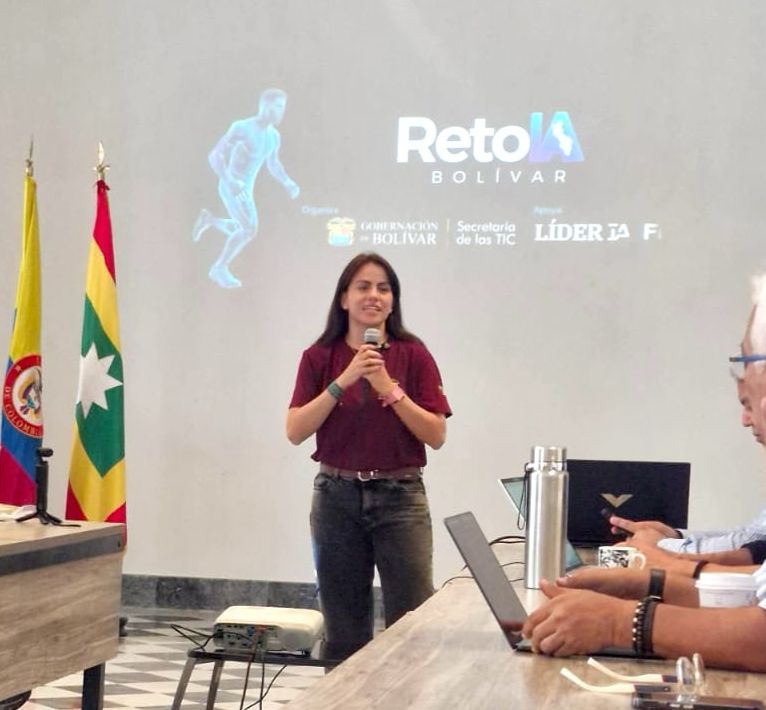 Mujer habla con micrófono frente a una pantalla del Reto IA Bolívar.