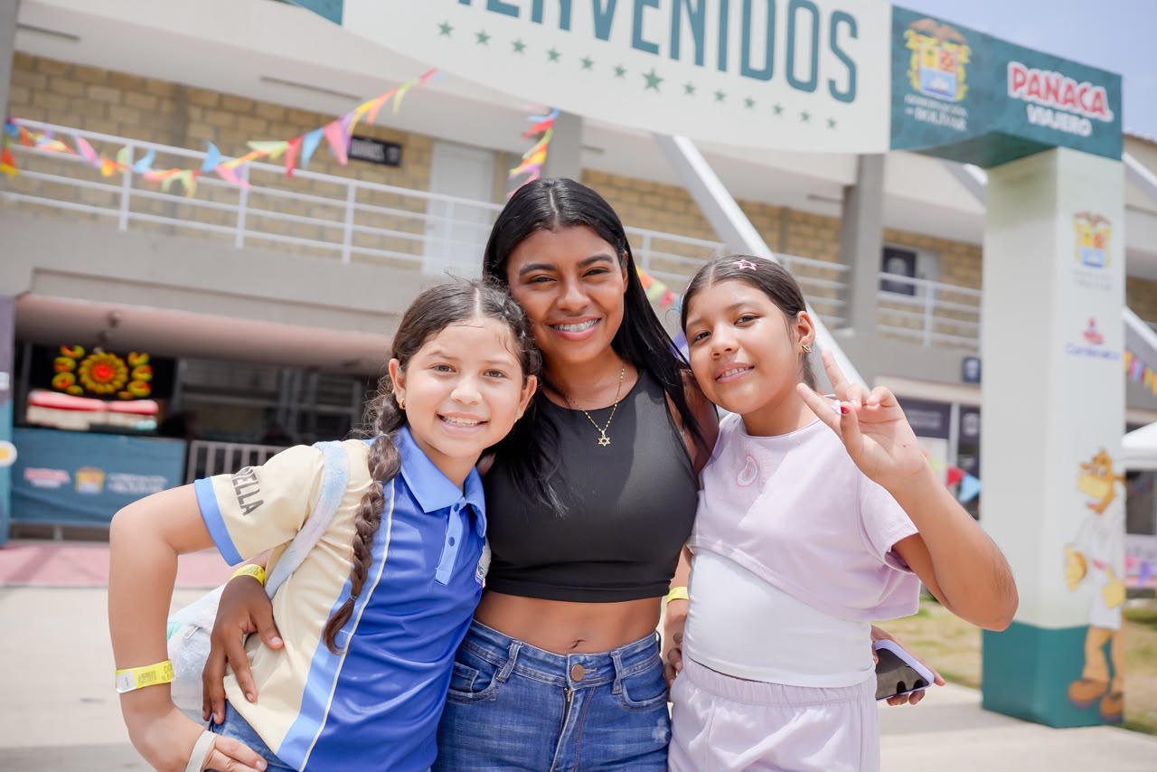 Tres niñas posan abrazadas frente al arco de bienvenida de Panaca Viajero.