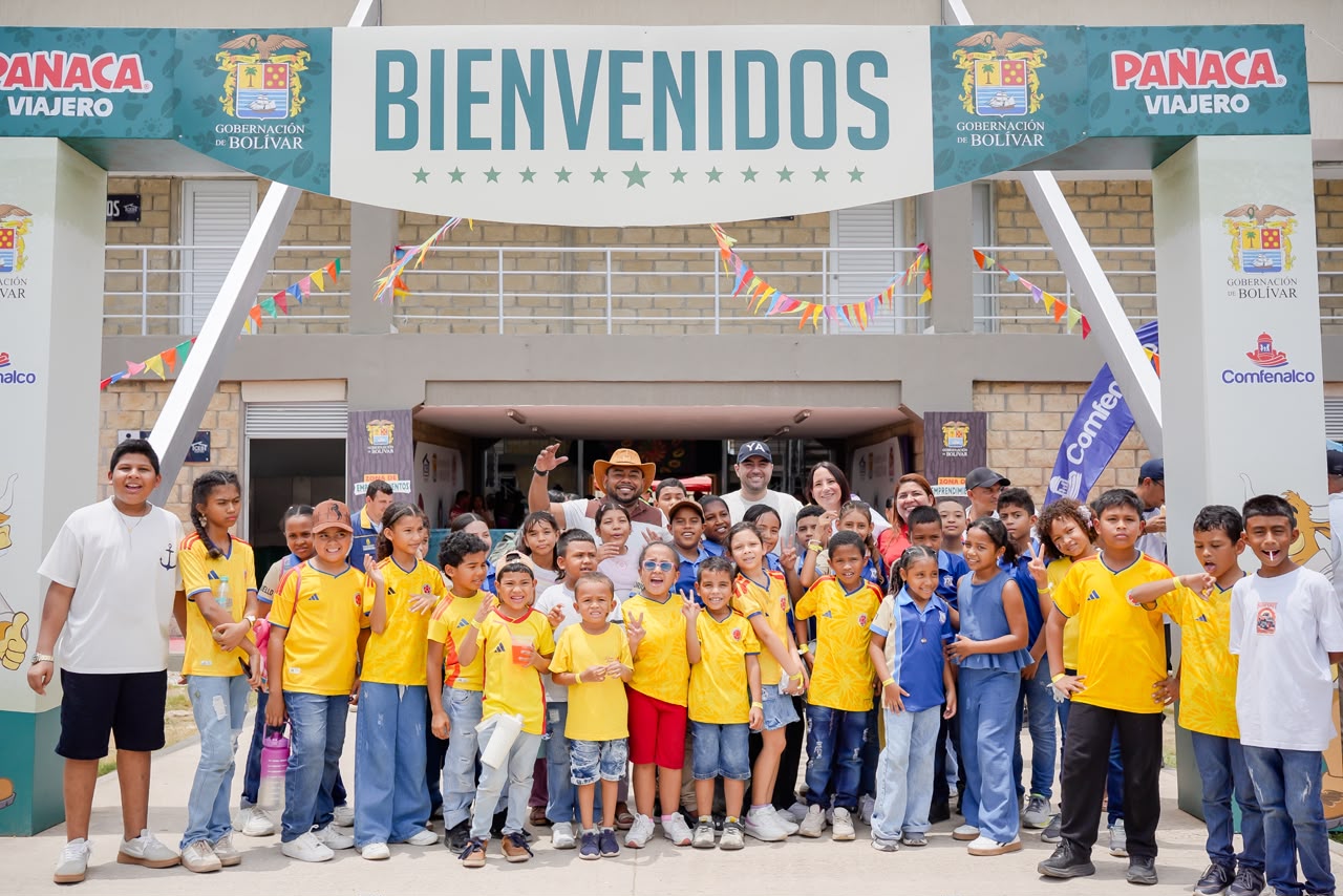 Grupo de niños y niñas con camisetas amarillas posa bajo el arco de bienvenida de Panaca Viajero.