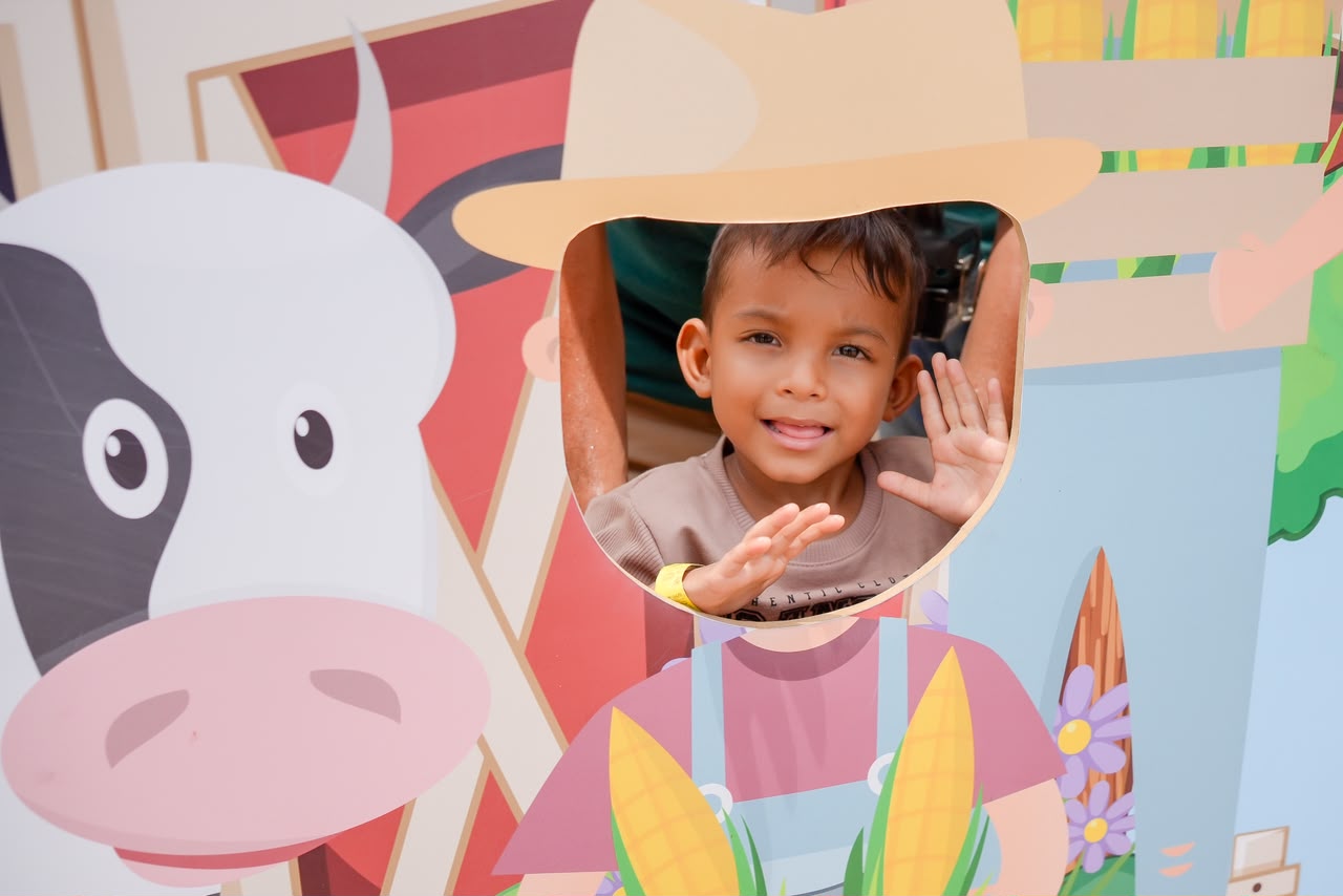 Niño sonriente asoma la cara por el hueco de un mural decorativo de granja.