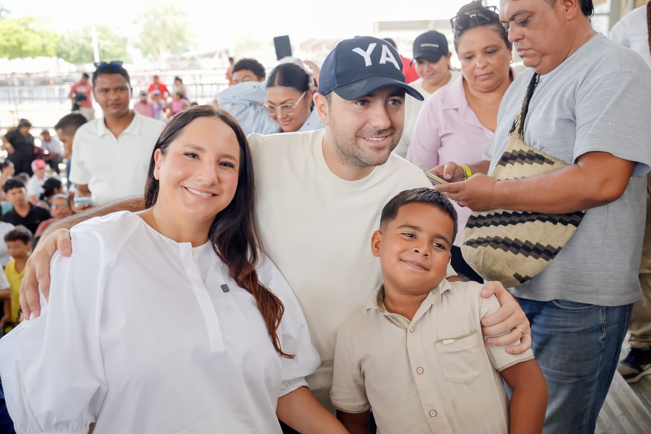 Un hombre y una mujer posan con un niño y otros visitantes en las graderías.