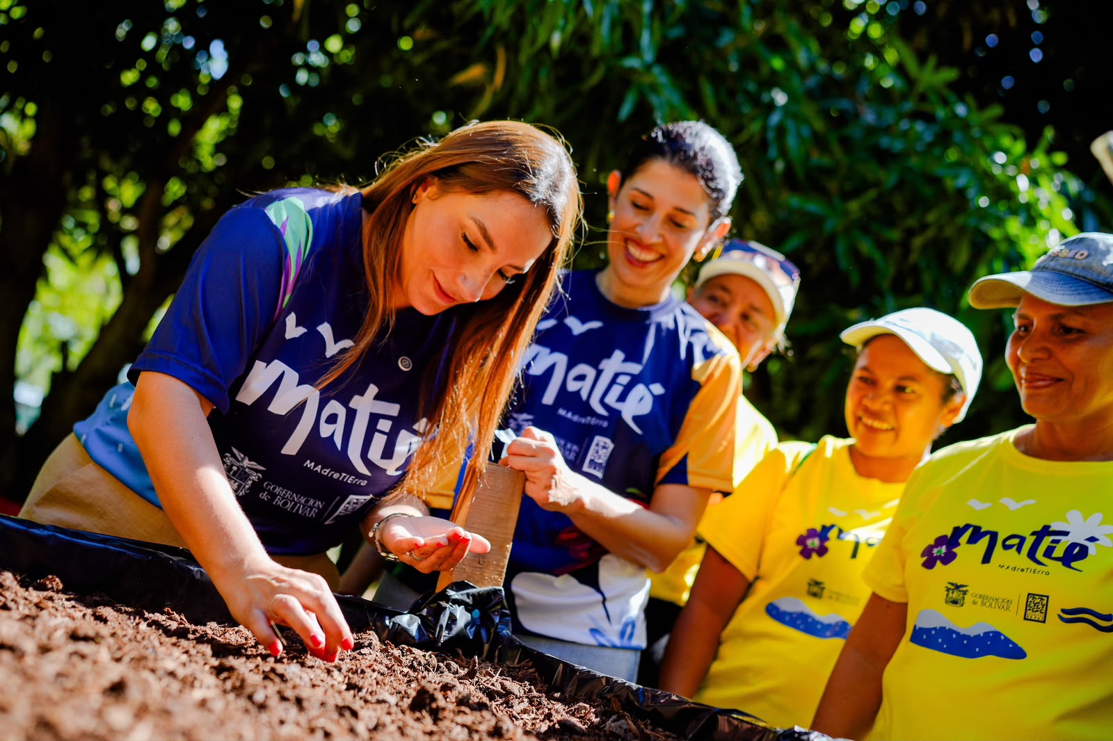 Mujeres con camisetas del proyecto MATIE trabajan con tierra en una actividad de siembra.