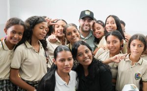 Grupo de estudiantes sonrientes con uniforme escolar posa junto a un hombre con gorra.