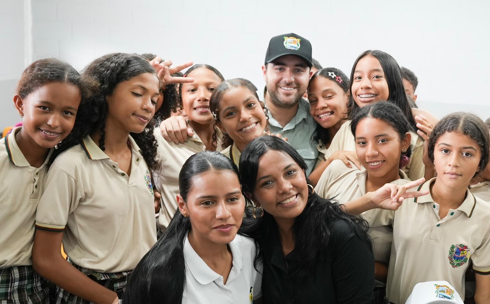 Grupo de estudiantes sonrientes con uniforme escolar posa junto a un hombre con gorra.