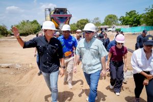 Grupo de personas con cascos recorre las obras del parador turístico en un terreno de arena.