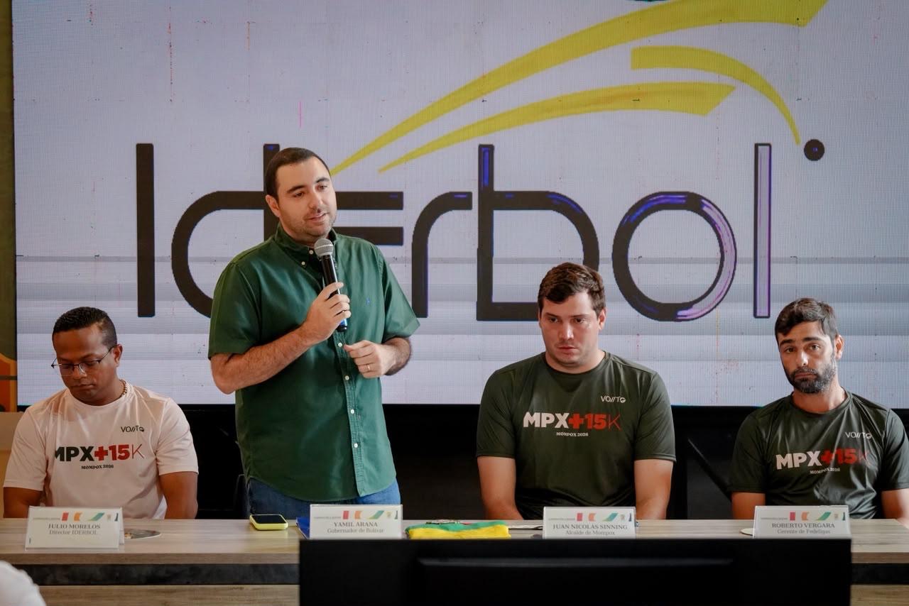 Hombre habla con micrófono en una mesa de rueda de prensa frente al logo de Iderbol.